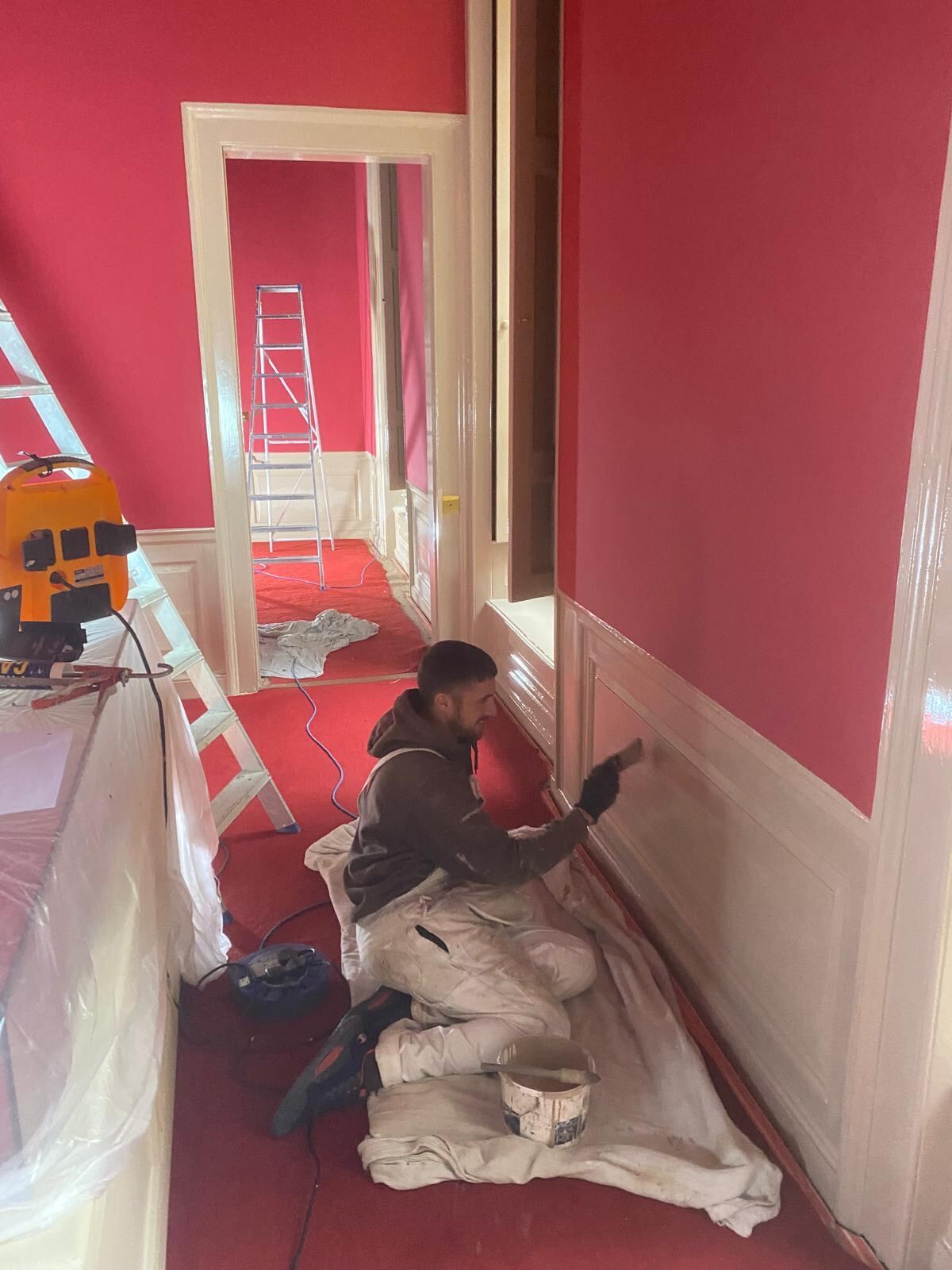 Brierty decorator painting white wainscoting in a heritage red state room at Blenheim Palace, Woodstock Oxfordshire